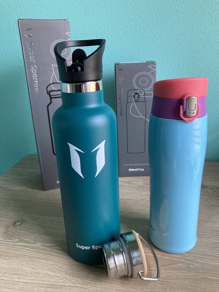 hard shell waterbottle in dark teal with black spout, blue and pink shiny waterbottle with press button mouthpiece