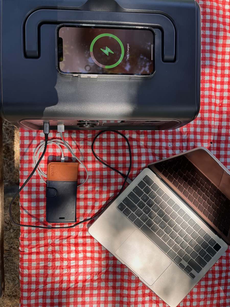 overhead of power station charging two phones and a laptop on checkered camping table