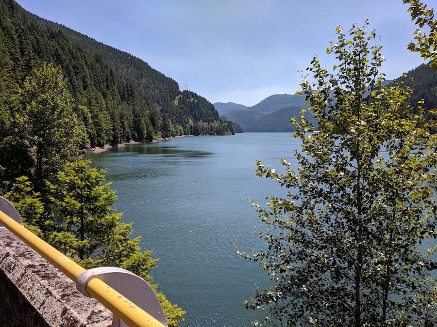 Scenic lake surrounded by lush green mountains in Central Oregon, viewed from a roadside lookout during a drive.