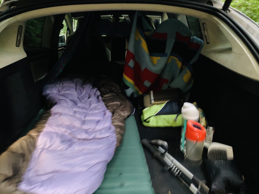 sleeping bag and privacy blankets set up in back of Tesla X