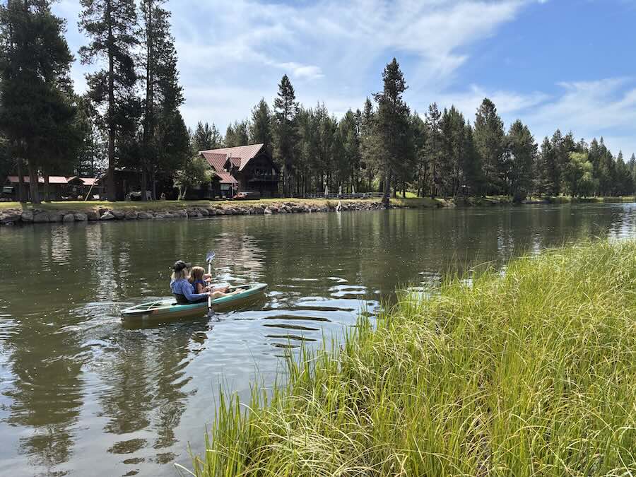 Deschutes river, two people kayaking with cabin and pine trees in background