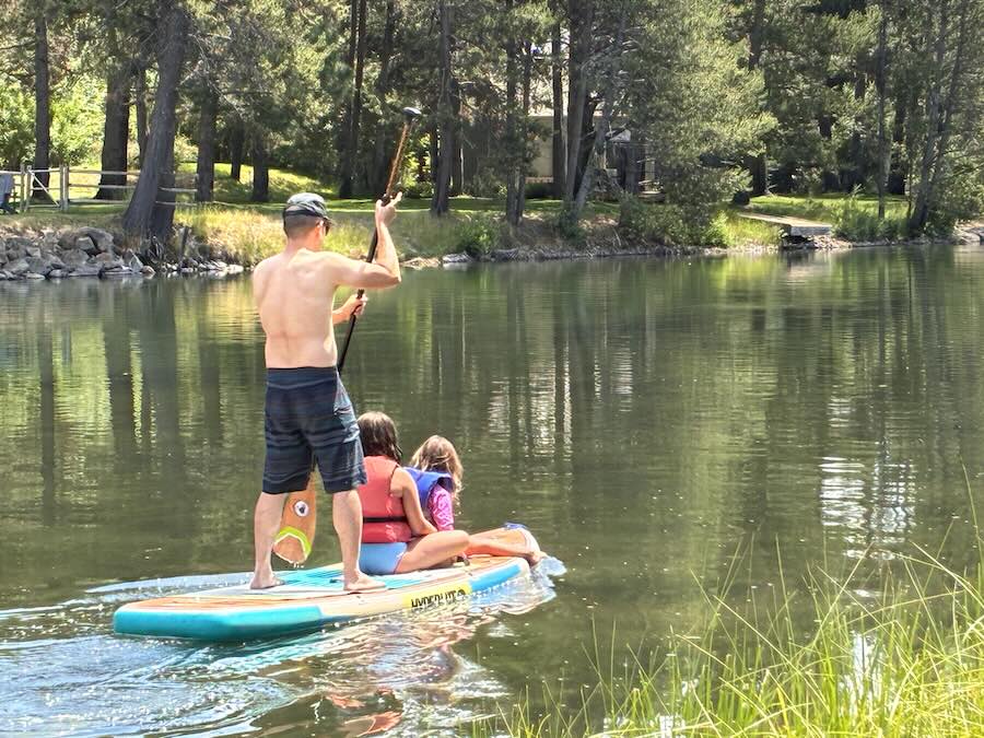 SUP with two kids riding in front on river surrounded by greenery